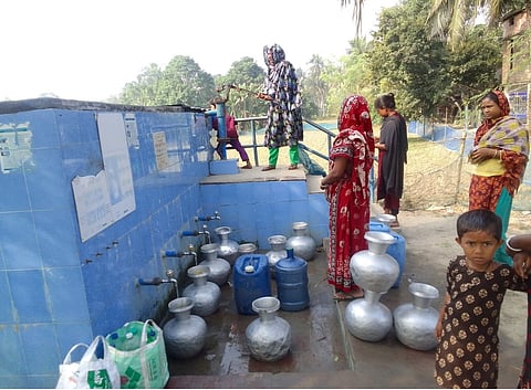 Villagers queue up at a pond sand filter. They complain that the system no longer works and the water isn't potable. 