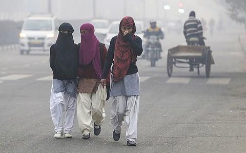 School children walk on the road, wearing masks to protect themselves from air pollution, as heavy smog envelops Delhi on a December morning.