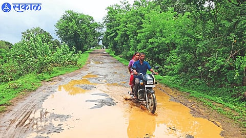 Khambale Mhasgan bike riding through potholes and stagnant water on the road.