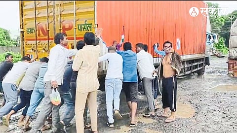 Passengers pushing out a vehicle stuck in a pothole on the Dhule-Surat highway.