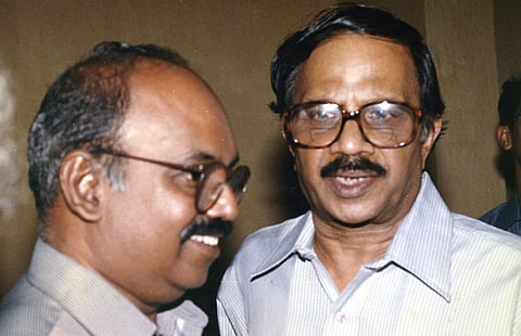 An old photograph of M T Vasudevan Nair (right), wearing glasses and a light striped shirt, smiling while facing the camera. K Ramachandra Babu (left) facing past the camera stands next to MT.