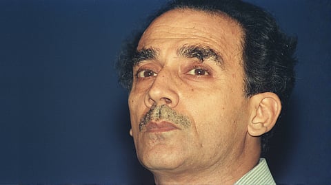 A close-up portrait photograph of Arun Shourie, looking slightly upward against a plain dark blue background. 