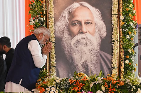 The Indian prime minister Narendra Modi bows with folded hands before a large garlanded portrait of Rabindranath Tagore, surrounded by flowers at a commemorative event.