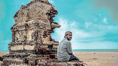 தனுஷ்கோடியில் சிதிலமடைந்த கோயில் இடிபாடுகள் மீது அமர்ந்து புகைப்படம் எடுத்த சுற்றுலாப் பயணி.