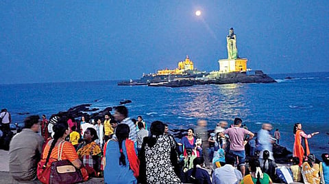 கன்னியாகுமரி முக்கடல் சங்கமத்தில் கடல் நடுவே ஓங்கி உயர்ந்து நிற்கும் திருவள்ளுவர் சிலையின் பின்னணியில் காலை நேர தெளிந்த நீலவானில் பிரகாசிக்கும் சூரியனை பார்த்து மகிழும் சுற்றுலா பயணிகள்.