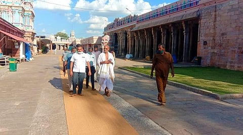 கோயிலுக்குள் விரிக்கப்பட்ட தென்னை நார் தரை விரிப்பில் நடந்துசெல்லும் கோயில் இணை ஆணையர் செ.மாரிமுத்து உள்ளிட்டோர்.