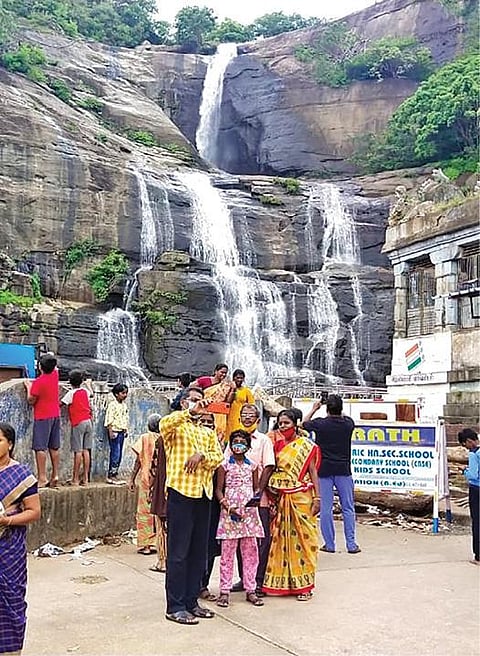 குற்றாலம் அருவிகளில் குளிக்க அனுமதிக்கப்படாததால் அருவி அருகில் நின்று புகைப்படம் எடுக்கும் பொதுமக்கள்.