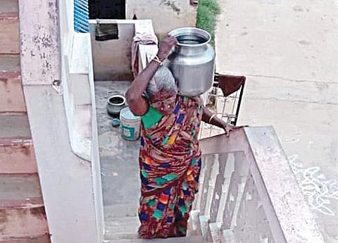 தண்ணீர் குடத்தை தோளில் சுமந்தபடி மாடிப்படி ஏறும் 105 வயது அச்சம்மாள்.