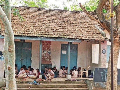 அங்குச்செட்டிப்பாளையம் உயர்நிலைப்பள்ளியில் பழுதடைந்த வகுப்பறைக் கட்டிடத்தில் அமர்ந்திருக்கும் மாணவர்கள்.