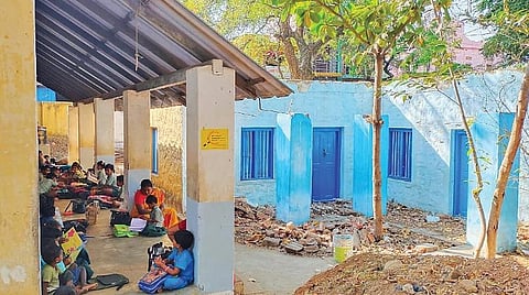 தளவாய்புரத்தில் வகுப்பறை சீரமைக்கப்படாததால் வராண்டாவில் அமர்ந்து படிக்கும் மாணவர்கள்.