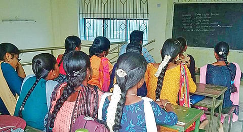 வகுப்பறை பற்றாக்குறையால் வராண்டாவில் பயிலும் மாணவ, மாணவிகள்.