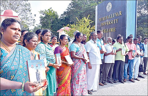 வேலூர் திருவள்ளுவர் பல்கலை. நுழைவுவாயில் முன்பாக `திருவள்ளுவர் பல்கலைக்கழகத்தில்  தில்லுமுல்லு' என்ற புத்தகத்துடன் பல்கலை. தொழிலாளர் சங்கத்தினர். படம்: வி.எம்.மணிநாதன்