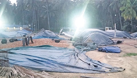 நெகமம் அருகே கொப்பரை களத்தில் மழையில் நனையாமல் இருக்க மூடி வைக்கப்பட்டுள்ள தேங்காய் கொப்பரைகள்.
