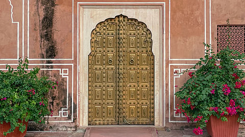 An intricate, handcrafted gold brass royal door in Jaipur India framed by vibrant pink bougainvillea flowers, highlighting majestic traditional Indian architecture