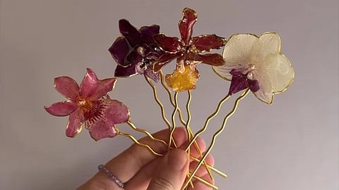 Hands applying clear resin to a fresh pink Phalaenopsis orchid with a paintbrush for DIY jewellery making.