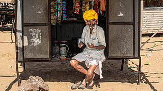 Elderly Rajasthani vendor with yellow turban at local market stall, rural India.