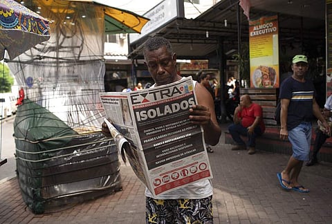 Rio de Janeiro, Brazil: A man reads a newspaper with the Portuguese headline, 'Isolated. Rio in war against coronavirus' in the Rocinha slum of Rio de Janeiro. (AP Photo/Silvia Izquierdo)