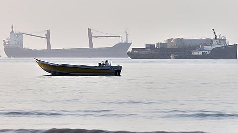 A small boat moves along the shoreline where an a cargo vessel
