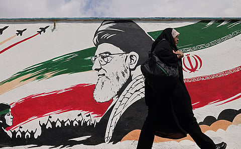 A woman walks past a wall mural of Iran's slain supreme leader Ayatollah Ali Khamenei, along a street in downtown of Tehran 