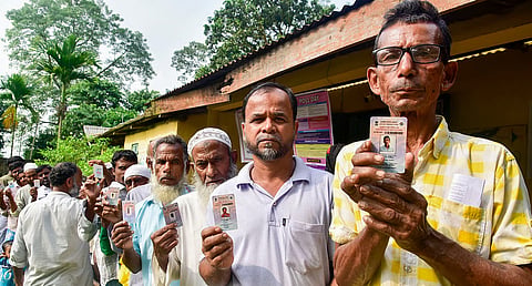 Voters display their voter identity cards as they stand in a queue to cast their votes at a polling booth during the Nagaon Lok Sabha 