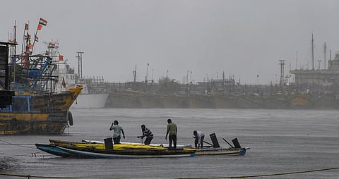 Fishermen secure their boats at a fishing harbour amidst heavy rain under overcast skies