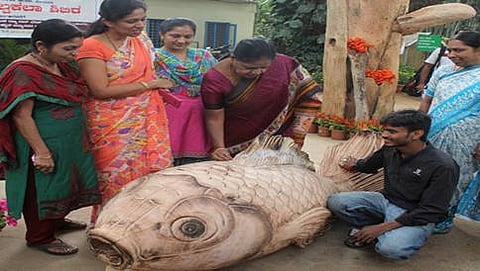 ಮರದ ತುಂಡಿನಲ್ಲಿ ಕೆತ್ತಲಾದ ಮೀನಿನ ಕಲಾಕೃತಿಯನ್ನು ವೀಕ್ಷಿಸುತ್ತಿರುವ ಕಲಾಸಕ್ತರು