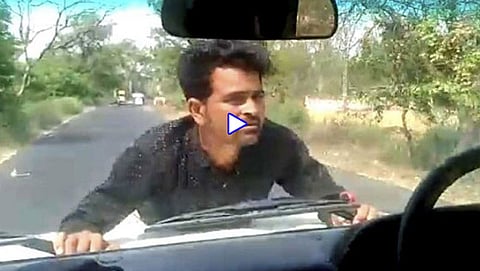 ಕಾರಿನ ಬ್ಯಾನಟ್ ಹಿಡಿದು ನಿಂತಿರುವ ಪ್ರತಿಭಟನಾಕಾರ