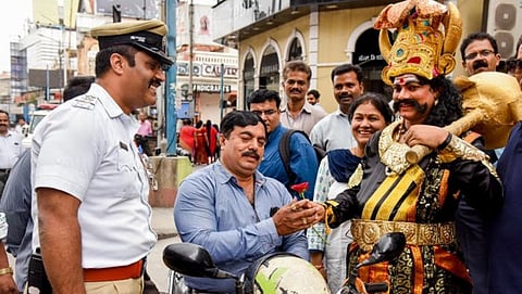 ವಾಹನ ಸವಾರರಿಗೆ ಗುಲಾಬಿ ಹೂ ನೀಡುತ್ತಿರುವ ಯಮ