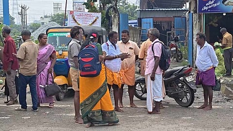 சாலை ஓரத்தில் பஸ்சுக்காக காத்திருக்கும் பயணிகள்