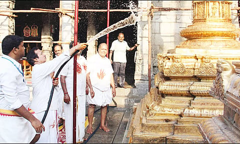 கோவில் அதிகாரி கொடி மரத்துக்கு தண்ணீரை பீய்ச்சியடித்து சுத்தம் செய்த காட்சி.