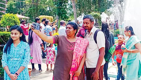 செயற்கை நீரூற்று முன் நின்று செல்பி எடுக்கும் சுற்றுலா பயணிகள்.
