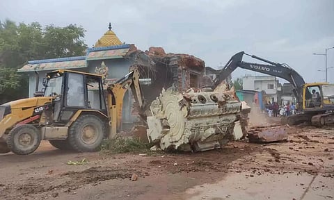 அம்மன் கோவிலை தேசிய நெடுஞ்சாலைத் துறை அதிகாரிகள் போலீசார் உதவியுடன் பொக்லைன் எந்திரம் மூலம் இடித்த காட்சி.