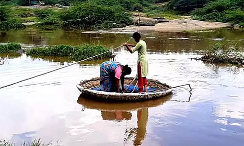 கம்பிகளை பிடித்து கொண்டு பரிசல் மூலம் ஆற்றை கடக்கும் பெண்கள். 