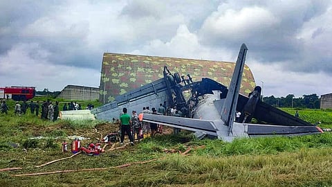 Security personnel and others stand near damaged remains of a transport aircraft of the Indian Air Force (IAF) that crashed while landing, in Jorhat district, Assam.