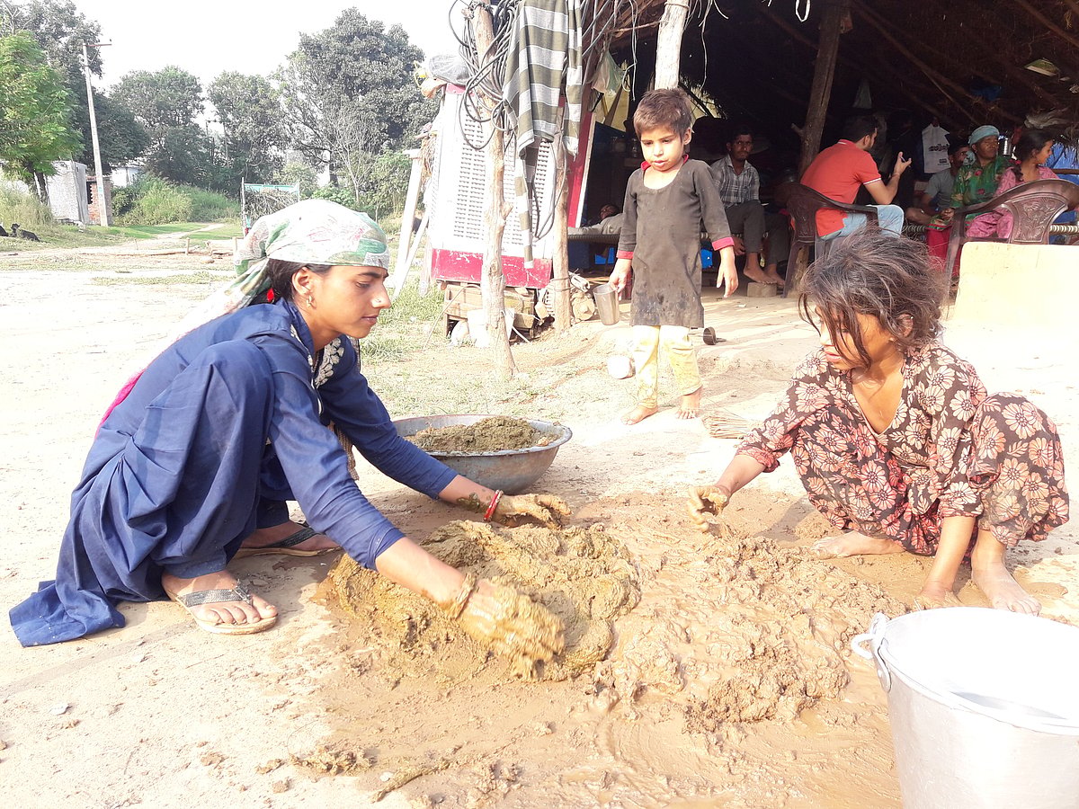 Tribal girls mixing mud and straw to make daub to put on the walls of their huts. 