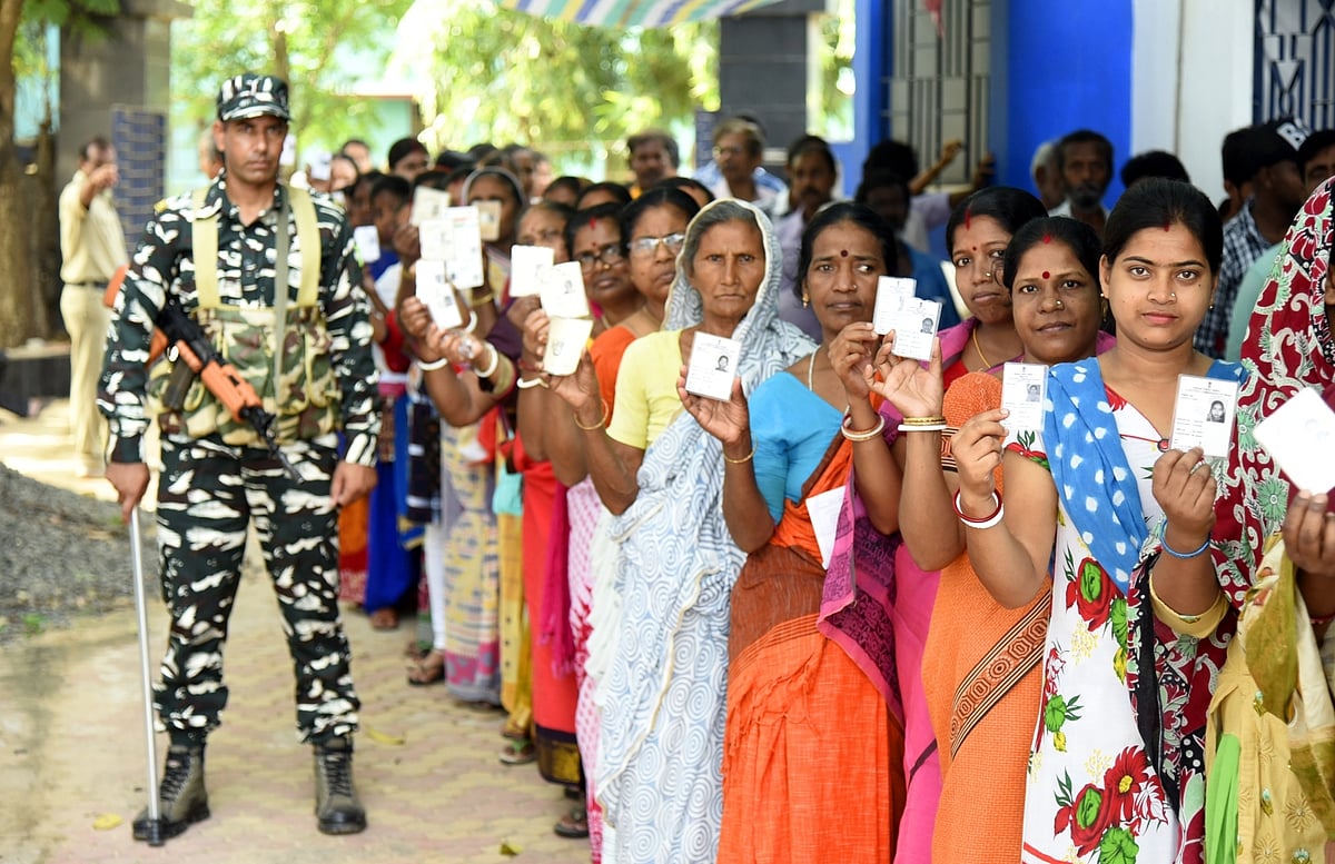  security personnel stands guard as women queue up to cast their votes for the fourth phase of 2019 Lok Sabha elections at a polling station at Bolpur in West Bengal’s Birbhum, on April 29, 2019 (IANS Photo)