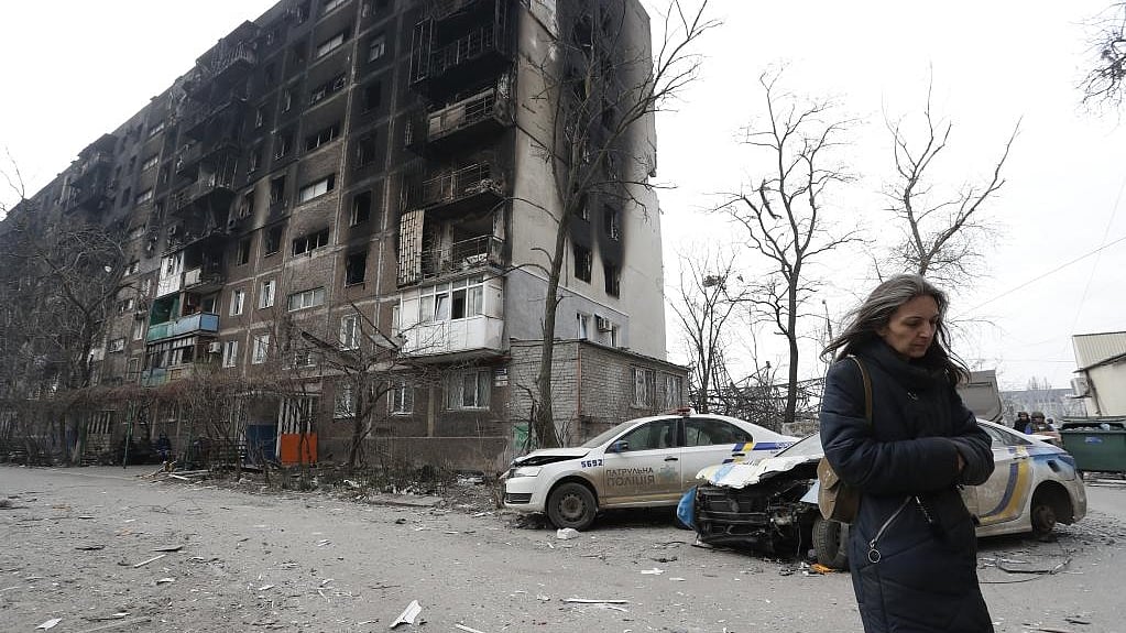 A woman walks past a damaged building in Mariupol