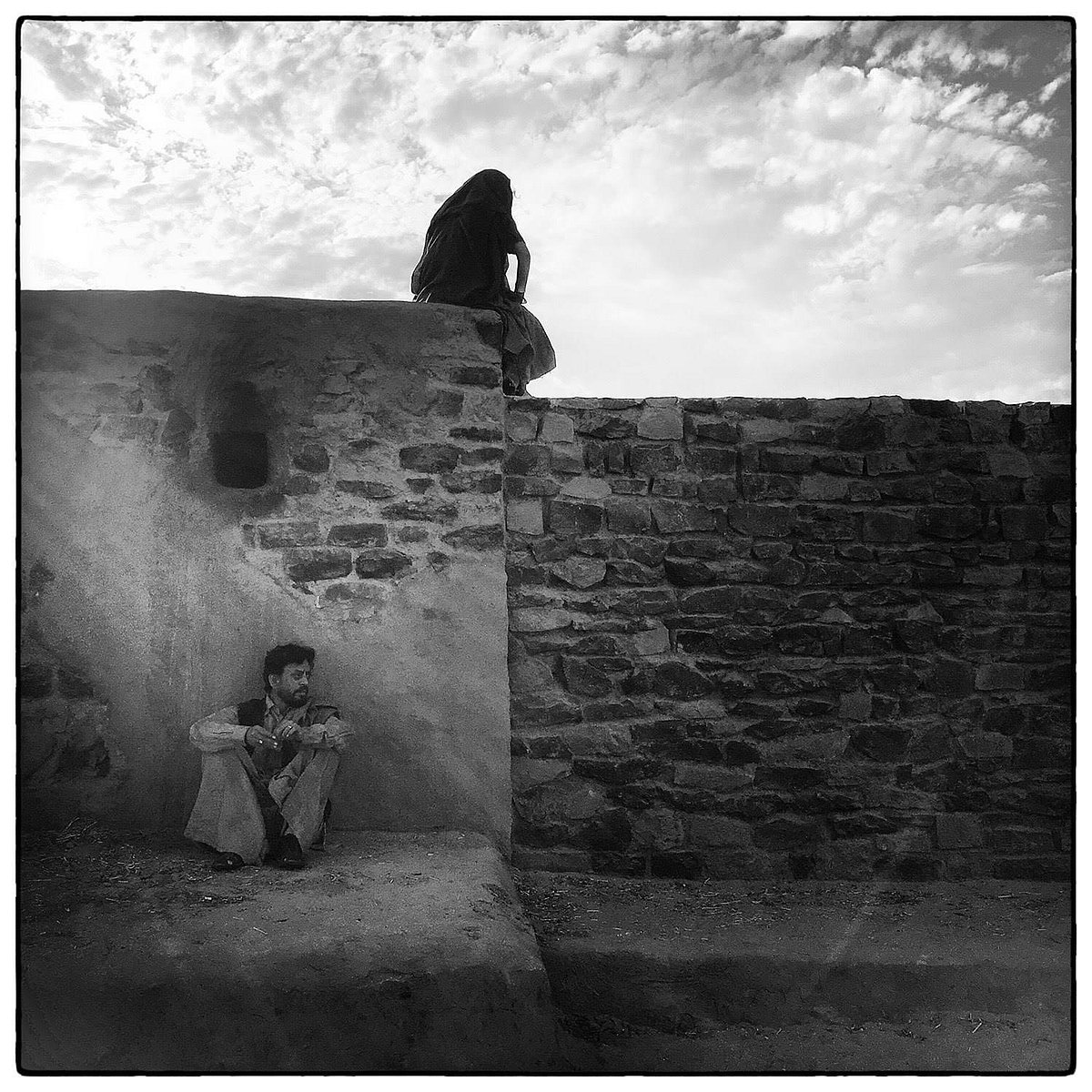 Irrfan sits with back to wall, on which a woman sits silhouetted (still from 'The Song of Scorpions')