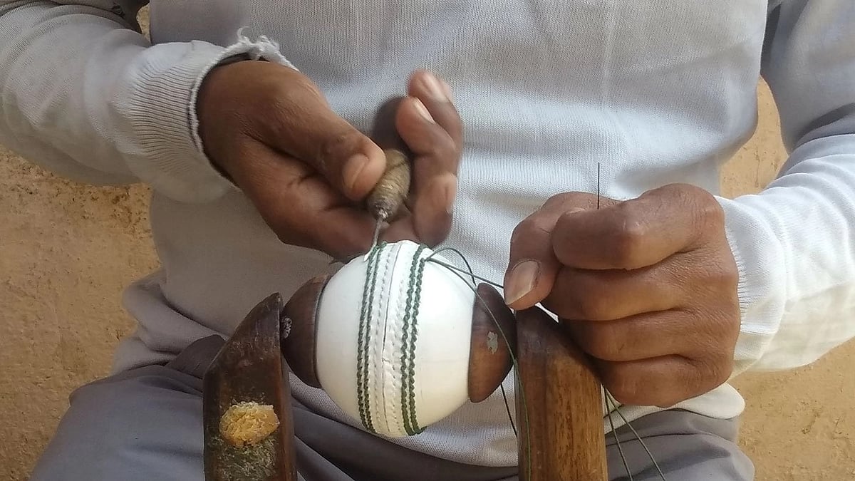 A worker stitches two pieces of a cricket ball together, a task that demands high skill