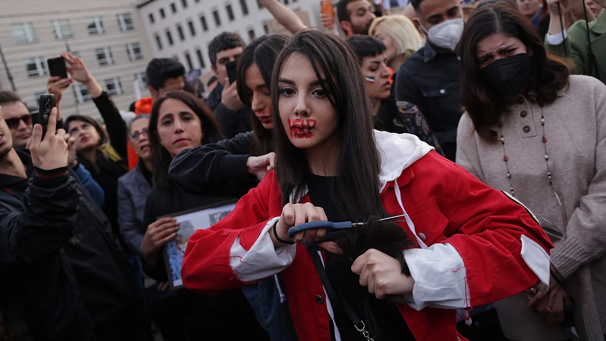 A protester in Berlin with 'help' written in red ink on her face cuts her hair during a 2022 protest rally against the death of Mahsa Amini, who was arrested for not wearing her headscarf properly (photo: Getty Images)