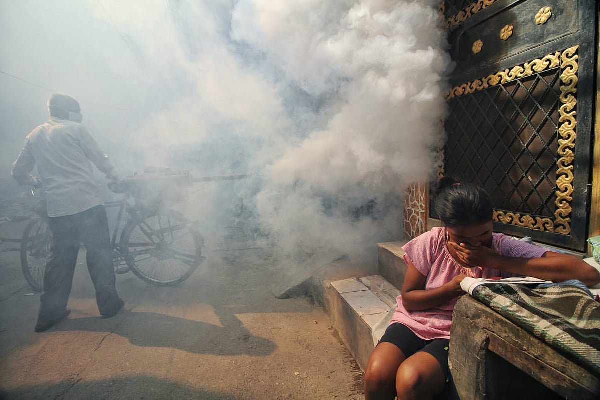 A worker carries anti-mosquito fogging equipment on his bicycle  through the colony, while children play and study in the streets. (photo: Vipin/National Herald)
