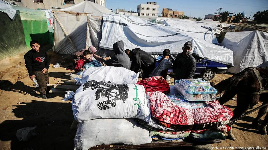 Families with young children at a refugee camp in Gaza, with makeshift tents made of sheets string over wires and cares, with a horse-drawn sled of sorts piled with household linens and bedding (photo: DW)