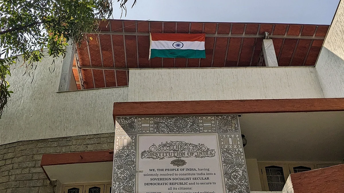 A large-sized print of the Preamble to the Constitution of India hangs from the terrace of a home, below the national flag, which flies near the roof (photo courtesy @bahudari/X)