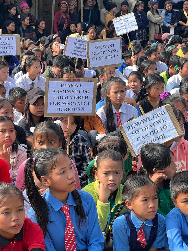 Children of 36 private and government schools sit-in in Moreh, Manipur, on 27 January 2024, many of them in uniform. Several hold placards calling to remove the "arsonist" CDO and call on Prime Minister Narendra Modi to ensure re-opening of schools. 