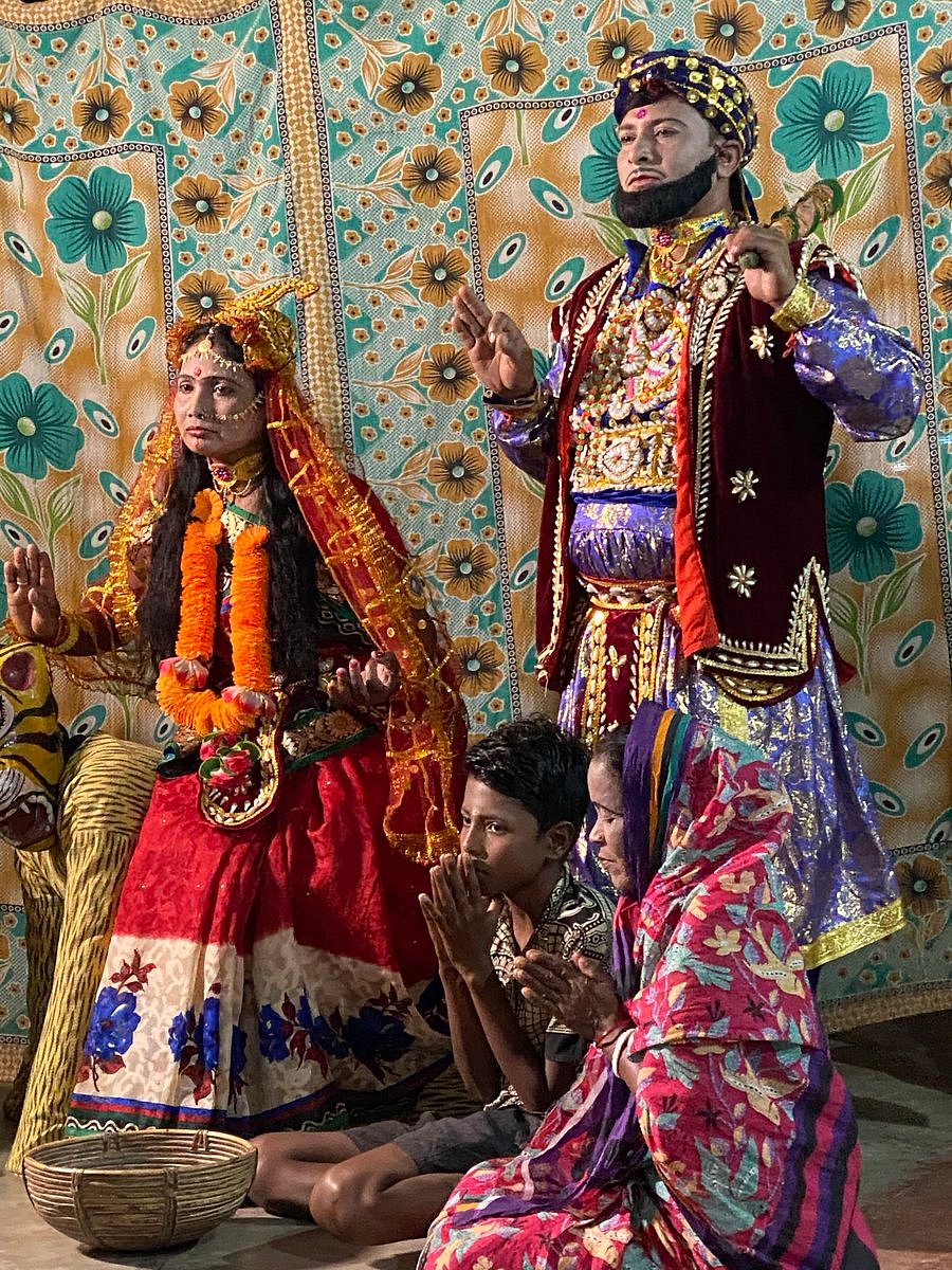 Bonbibi (seated, left), Muslim–Hindu syncretic goddess of the forest, is worshipped in a play enacting her legend with Dokkhin Ray, the tiger demigod, kneeling behind her. Beside her (right) stands her twin brother Shah Jangali, the 'king of the jungles'. At their feet sit the child Dukhe (unfortunate one) with his mother.