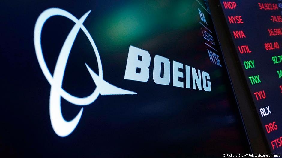 Representative image of the Boeing logo on a board next to an airport flight schedule screen (photo: DW)