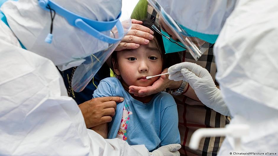 Small Asian-origin child being checked for Covid-19 by adults in protective gear (photo: DW)