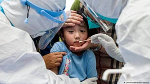 Small Asian-origin child being checked for Covid-19 by adults in protective gear (photo: DW)