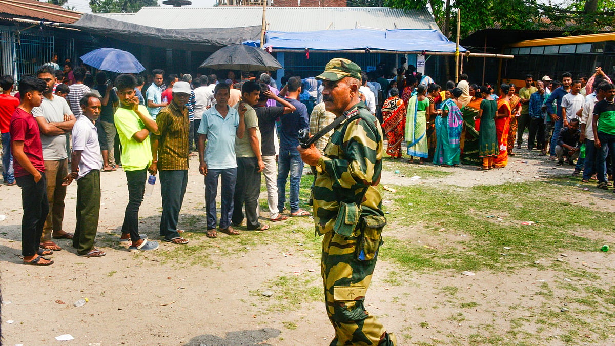 A security personnel stands guard as voters wait at a polling station in Jalpaiguri on 19 April (photo: PTI)