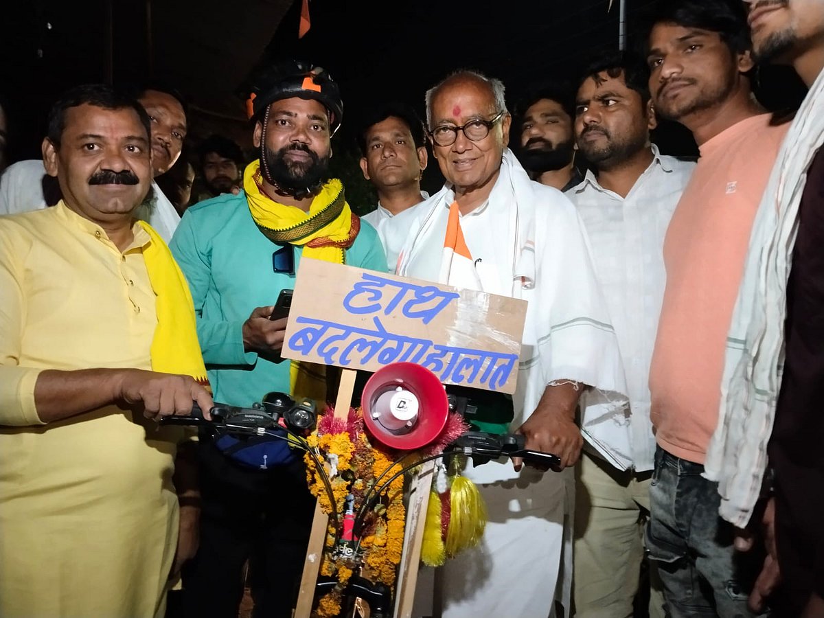 An Adivasi supporter with Congress veteran Digvijaya Singh, seen here campaigning on a bicycle, carrying the placard 'the hand will bring change', in the evening (photo courtesy @AdvSuneelkumar/X)